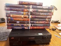 Photo of the VCR player with a stack of Disney VHS tapes arranged horizontally and vertically around it showing titles and brand information.