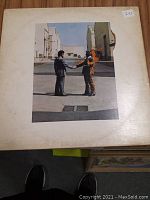 Front cover of Pink Floyd "Wish You Were Here" vinyl album showing two men shaking hands, one on fire, with worn edges and discoloration on sleeve.