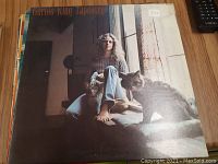 Front cover of Carole King 'Tapestry' vinyl record showing Carole King seated barefoot next to two cats by a window.