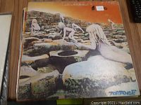 Front cover of Led Zeppelin album Houses of the Holy showing ethereal figures climbing rock formations with wear on cover edges.