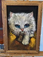 Frontal view of the black velvet painting showing the white kitten with large blue eyes and original wooden frame.