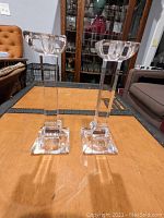 Full view of the pair of glass candlesticks standing on a table, showing height and shape.