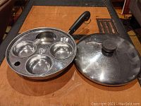 Egg poaching pan and lid placed on wood surface showing three egg cups inside pan, with one cup missing to the right side.