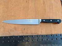 Top view of entire knife laid flat showing blade and handle details, taken on wood surface with decorative leather strip below.