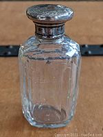 Clear glass cologne bottle with vertical cut facets and sterling silver hand chased lid with detailed engraving