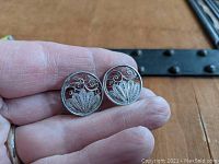 Photo shows the front side of both round sterling silver filigree screw-back earrings held between fingers to show size and detail.