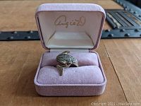 Ring displayed in pink velvet box, showing dolphin design with clear stones and red eyes