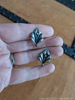 Close-up photo of both earrings held between fingers showing front detail