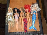 Five dolls laid out on a surface showing full bodies and outfits or lack thereof