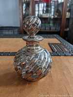 Close-up image of the antique glass cologne bottle with sterling silver overlay and matching stopper showing swirled texture and design details.