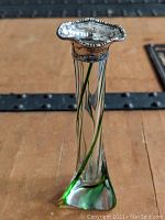 Front angle view of the bud vase showing the triangular shape, clear glass with green swirls, and sterling silver mounted rim.