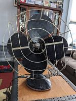 Front view of the antique electric fan showing black metal blades and protective silver metal cage.