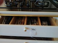 Drawer open showing wooden kitchen utensils organized in compartments, including wooden spoons, rolling pin, spatulas, whisks, and other metal kitchen tools.