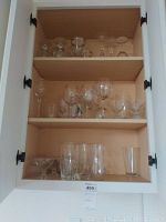 Image of three shelves inside a cabinet showing assorted glassware including wine glasses, water glasses, brandy sniffters, dessert glassware, and assorted clear glass drinking glasses.