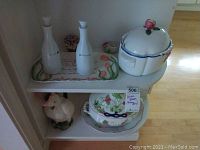 Shelf with two white ceramic decanters labeled 'Olive' and 'Vinegar' on a floral tray, covered serving dish with floral decoration, and bird-shaped water pitcher