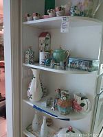 Shelf display of various ceramic and glass decorative items including mini flower pots, pitchers, vases, and figurines.