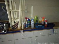 Wide view of assorted cleaners, tools, and a white wooden stool showing variety of cleaning liquids and maintenance sprays