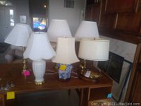 Front and side overview of all six lamps on wooden desk showing varying base materials and lampshades