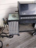 Close-up photo of the black Weber propane grill showing the side table with a glass top and the Weber logo on the grill lid.