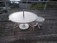 Photo of a white oval patio table and matching square end table with clear glass tops on a wooden deck outdoors.