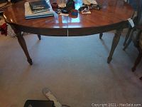 Full view of oval wooden dining table showing top surface, legs, and overall structure. Contents on top not included.