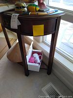 Front and side view of semi-circular wooden sofa table showing drawer, ornate handles, and adjacent smaller table with conical lower shelf underneath.
