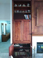 Wide view of wood cabinetry with ceramic village figurines on upper shelves and hardback books below.