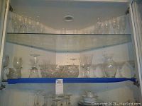 Shelf showing clear wine glasses in various styles on the top shelf, cut glass bowls and vases on the middle shelf