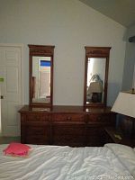 Front view of wooden dresser showing nine drawers and two vertical mirrors with decorative tops.
