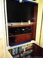 Vizio flat-screen TV mounted inside wooden cabinet showing Panasonic VHS/DVD player below and lower compartment of books.