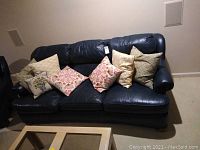 Full view of the blue leather sofa with all six throw pillows arranged across seating area