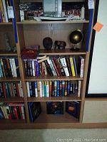 Bookshelf with hardback books, brass decorations including globe, wooden carved mask, small wooden house figurines, and a brass elephant figurine