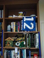 Full bookshelf showing multiple shelves packed with sports books, Packers memorabilia, and a flag.