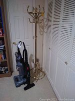 Photo showing brass coat rack beside Hoover vacuum and upright sweeper on carpeted floor.