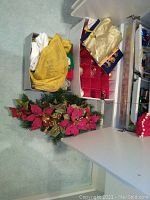 Wide view of shelves and floor showing holiday decorations, including poinsettia arrangement and gold ribbons in boxes