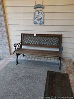 Photo of outdoor bench with metal lattice back and wooden seat, situated near a brick wall.