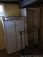 Three portable fabric closets with black trim, standing in a basement corner, showing zippered fronts and different sizes.