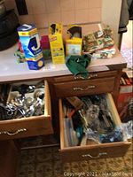 Drawer with various silverware and scissors visible including spoons and forks, kitchen paper products visible on countertop.