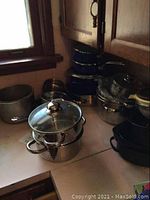 Overall view of kitchen counter with stacks of pots, roasting pans, and bowls.