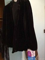 Front view of the black faux fur jacket hanging on a hanger, showing the texture and silhouette.