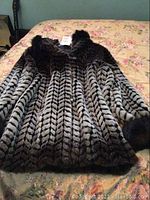 Full view of ladies Sequence faux fur jacket laid flat, showing black and grey chevron pattern and darker collar and cuffs.