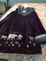 Full front view of the purple ladies jacket laid flat on floral bedding showing bear silhouette pattern and fur trimmed collar and cuffs.