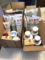 Photo showing two open boxes filled with various Kalaya products including tubes of pain relief cream, hair health shampoo, jars of moisture cream and skin salve, and multiple bar soaps.