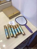 Six unopened Elizabeth Grant serum bottles and a handheld mirror on countertop