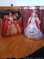 Two Holiday Barbie dolls in original display boxes. One doll wears a red and gold gown; the other wears a silver and white gown with red fur cape.