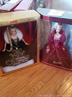 Two original boxed Holiday Barbies from 2002 and 2006 displayed side by side on hardwood floor.