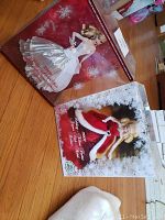 Two boxed collector Holiday Barbie dolls displayed on wooden floor, one in red/white outfit, the other in silver/white gown.