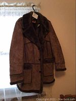 Full view of brown suede ladies jacket hanging on a black hanger, showing the entire front side including large collar and buttons, with dark faux fur trim.