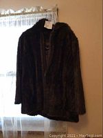 Photo of the front view of brown faux fur ladies jacket hanging near a window.