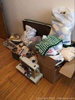Full view of Kenmore sewing machine and surrounding sewing accessories including bags and boxes of fabric and thread